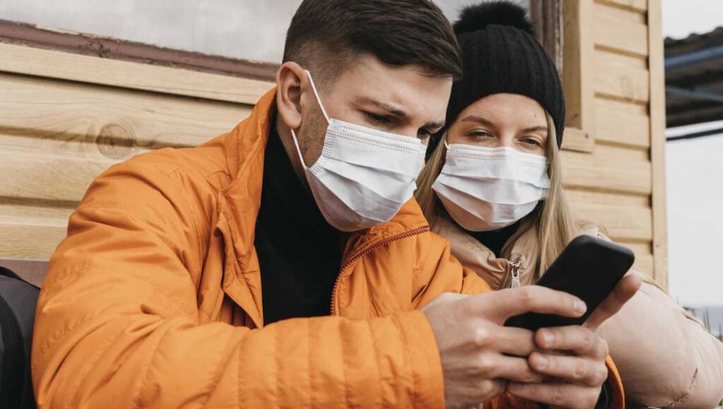 Foto de um casal com mascara olhando pesquisando no celular
